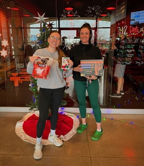 Two women holding pet donation items outside Orangetheory Fitness in Mason, Ohio during a holiday drive