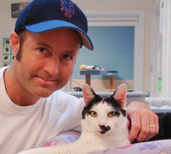 Volunteer wearing a baseball cap posing with a black and white cat.