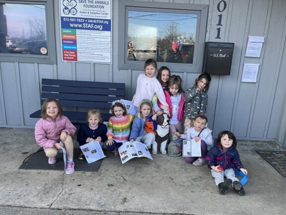 Group of volunteers and children outside the Save the Animals Foundation shelter, smiling and holding activity sheets.
