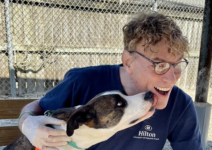 Corporate Volunteer cuddling a brown-and-white dog, with a kennel fence in the background.