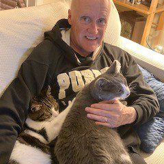 Smiling volunteer cuddling two cats on his lap.