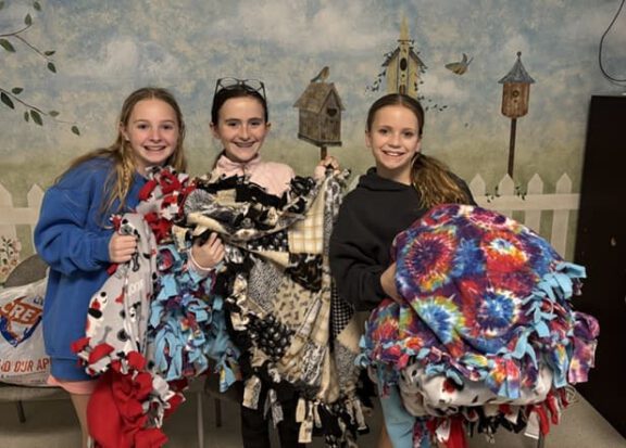 Three shelter volunteers hold colorful blankets donated to keep cats and dogs warm.