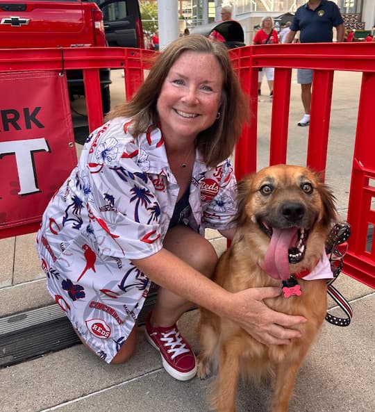 Save the Animals Foundation volunteer kneels beside a happy brown dog at a shelter event.